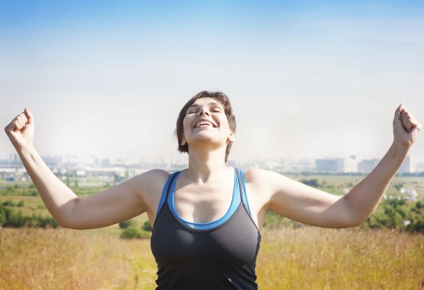 Happy beautiful successful plus size woman raising arms to the sky outdoor in summer